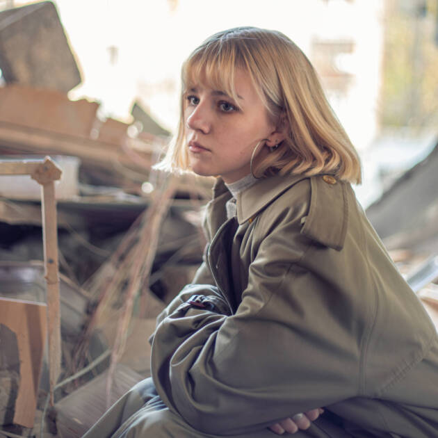 A woman near a house destroyed by the war. War in Ukraine. Ukrainian refugees. High quality photo. Peace concept. Sad girl near a destroyed house in Kyiv. Space for text.